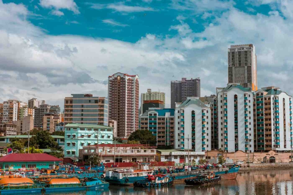 manila waterfront skyline with residential buildings, docked boats, and a calm river under a cloudy sky.