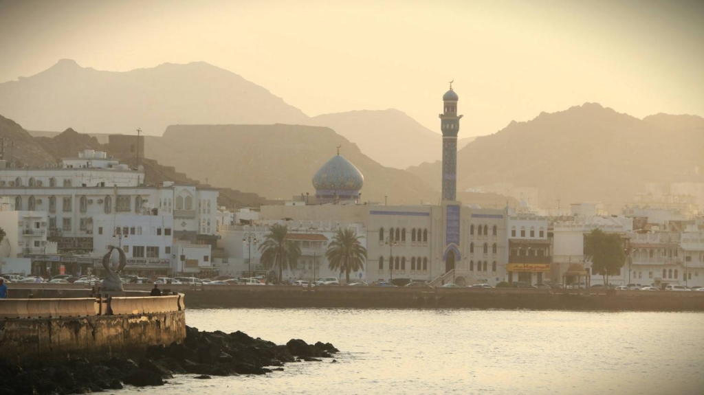 coastal cityscape in oman with mosque, waterfront, and mountains at sunset