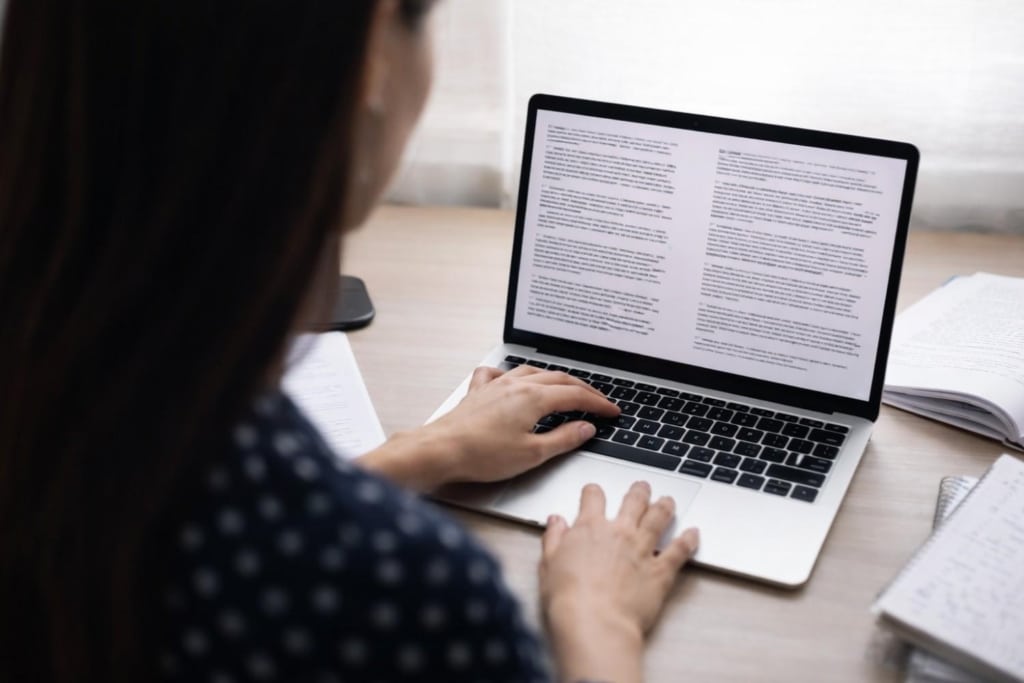 real estate article writing on a laptop with a person reviewing content at a desk.