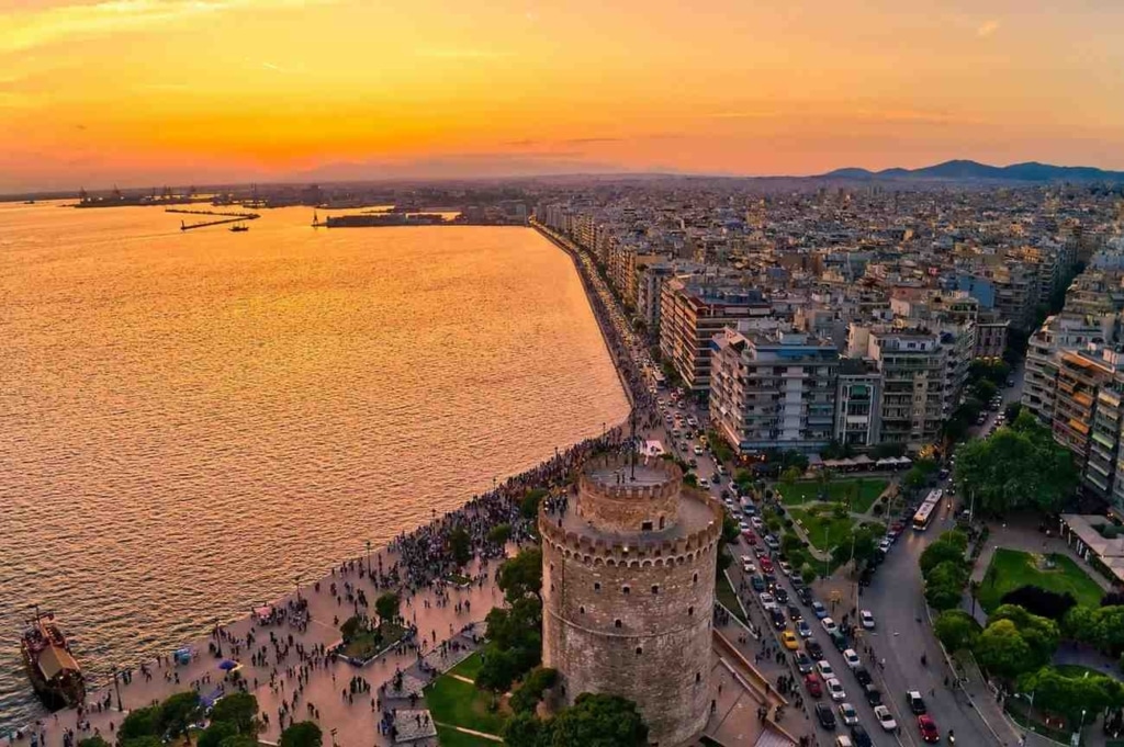 cheap houses in greece near a coastal city skyline and historic tower at sunset.